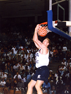 Photograph of a men's basketball player dunking during a game