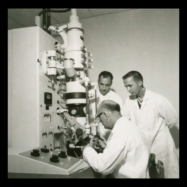 Image of students and a faculty member working with an early electron microscope