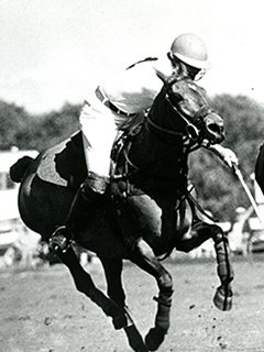 Photograph of a student riding a horse, playing polo